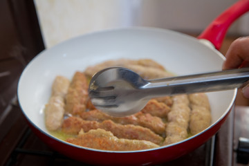 The long cutlet is fried in a red pan. She cooks the cutlet in a white pan.