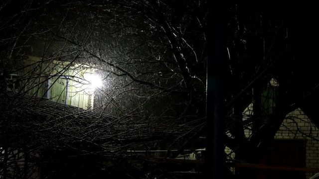 Snowfall in backyard of old house and light of lantern at night. Mysterious winter rural landscape. Medium plan.