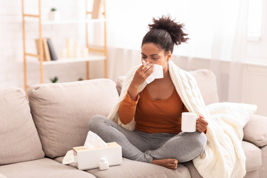 Sick Afro Woman Blowing Nose In Tissue Sitting On Sofa