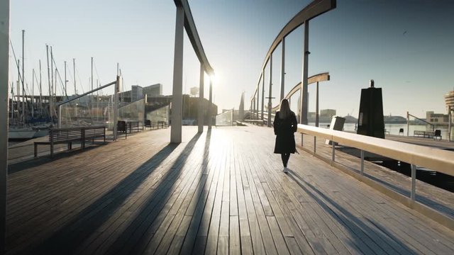 stylish  girl with sunglasses is walking into the sunrise in the harbor of Barcelona in Spain