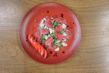 Restaurant food served on a red plate. Fish, cheese, salad, vegetables, sauce.