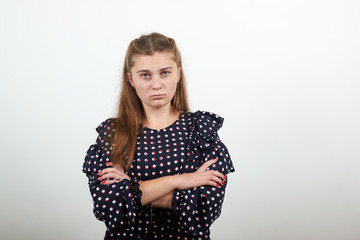 Fair-haired beautiful girl in a black dress with white circles looks nervously with an angry expression and clasped hands