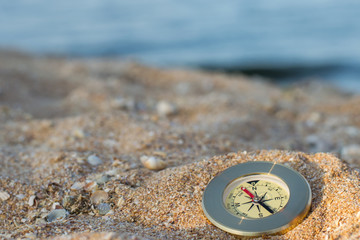 A compass showing the direction lies on the sea sand with shells