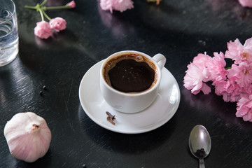 Fresh made coffee in white little cup on black table. Still life coffee cup, Glass of water,Sakura blooming flowers,Garlic bulb.Morning coffee.