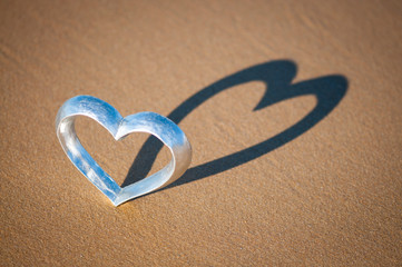 Shiny silver heart standing on the beach casting a shadow on textured sand