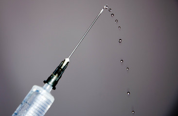 Syringe with a needle on a gray dark background. A drop, a stream flows from a syringe needle....