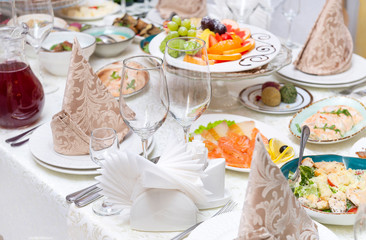 served holiday table with dishes, glass glasses, plates with appetizers, pieces of fish, salmon, fruit, salad, napkins,