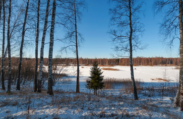 View from a high bank to a wide river covered with ice on a clear sunny winter day