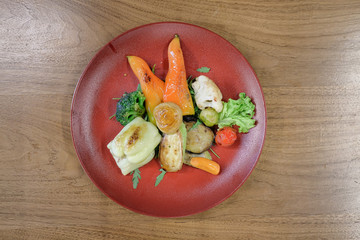 Restaurant food served on a red plate. Fish, cheese, salad, vegetables, sauce.
