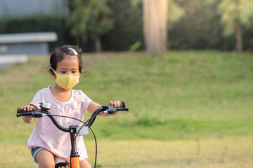 Little girl wearing anti pollution mask on her bike at park.