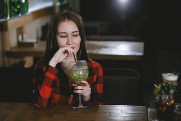 Young woman drinks a cocktail from a glass.