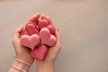 Woman hands holding many pink macaroons in the heart shape