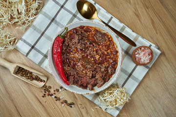 A traditional Mexican dish is chili con carne soup with stewed beef in a composition with spices on a wooden background. Tasty food photography