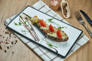 Appetizing vegetarian food - baked stuffed eggplant with pesto sauce and olive oil on a ceramic plate on a wooden background. Close up food
