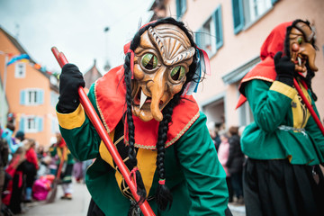 Freiburger Hexen - Hexe mit Katzenaugen im  grün, gelb, rotem Gewand mit schwarzen Zöpfen. Bei...