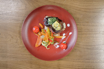 Restaurant food served on a red plate. Fish, cheese, salad, vegetables, sauce.