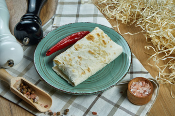 Spicy burrito or shawarma on a blue plate with different traditional fillings in a composition with spices. Close up view.