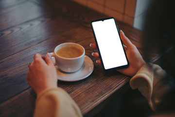 Mockup of woman holding smartphone with blank screen in cafe near tea cup
