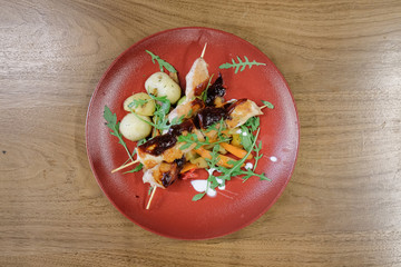 Restaurant food served on a red plate. Fish, cheese, salad, vegetables, sauce.