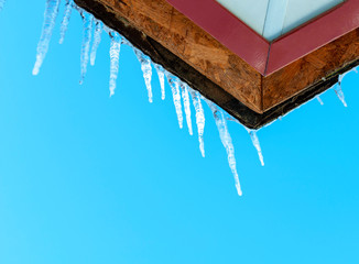Icicles on the roof of a house against a blue sky with copy space