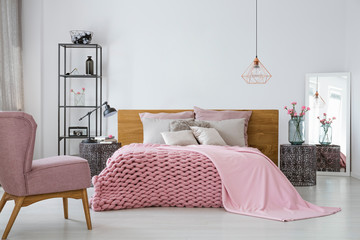 Pink cozy woolen blanket and duvet on king size bed in contemporary bedroom interior, copy space on empty white wall