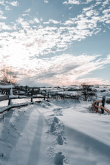Winter season, landscape picture of a village covered by snow at sunset, country landscape with timber fence