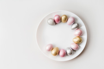 Colored painted pearl chicken and quail eggs of pink, silver, golden color on a purple plate pastel background. Minimalistic creative idea easter festive flat lay. Copyspace for text