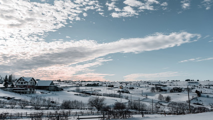 Winter season, landscape picture of a village covered by snow at sunset, country landscape with timber fence