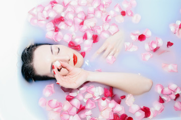 Obraz na płótnie Canvas Young sexy girl taking a milk bath with rose petals closeup