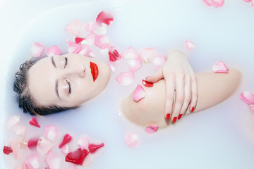 Obraz na płótnie Canvas Young sexy girl taking a milk bath with rose petals closeup