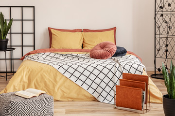 Black wooden grille next to the bed with orange bedding in the bedroom with white walls