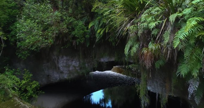 4k descending and backward tracking aerial view of Moria Gate Arch on the Oparara River in the Oparara Basin Arches situated in the Kahurangi National Park,Karamea,South Island New zealand