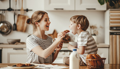 preparation of family breakfast. mother and child son cut bread  and eat cookies with milk in...