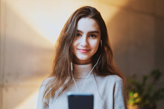 Beautiful girl listening to music in earphones. Young female model with long hair and pretty face posing at photo session. Great apps and entertainment online channels for downloading.