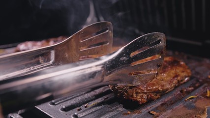 Delicious juicy meat steak cooking on grill. Aged prime rare roast grilling marble beef. Electric roaster, rosemary black pepper, salt. Kitchen tongs.
