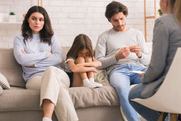Unhappy Parents And Their Upset Little Daughter Sitting At Psychologist's Office