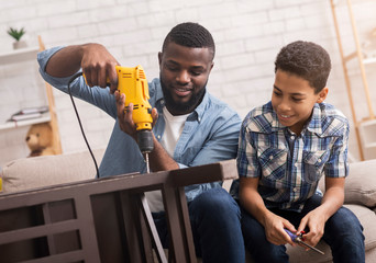 Black father teaching his son how to use drill perforator