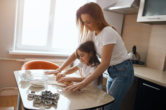 good looking blonde woman in white T-shirt and jeans teaching the child to use rolling pin, close up side view photo