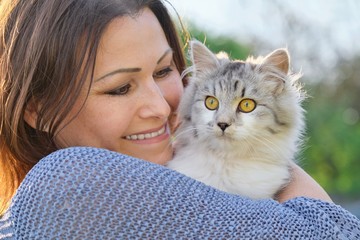 Portrait of mature woman with gray fluffy cat. Female holding pet in her arms