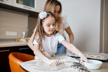 little girl going to pour some flour on the kitchen table. mommy standing behind and controlling her. close up photo