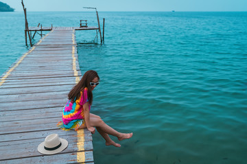 tourist a girl in the colorful shirt and sunglasses by sit relaxing on the walkway bridge wood in the sea in holiday for vacation trip form her with smile happy time relax day in the sea