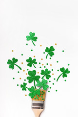 Creative St. Patricks Day greeting card. Paint brush with green glitter shamrocks and confetti. Minimal St. Patricks Day greeting card