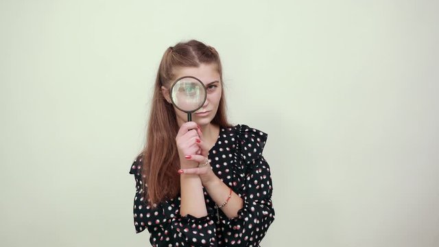Fair-haired beautiful girl in a black dress with white circles happy woman looks through magnifying glass magnifier