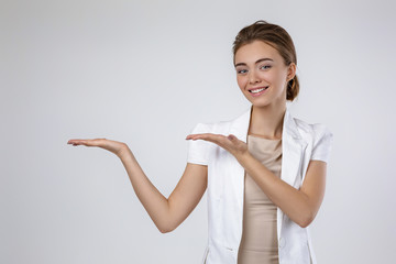 smiling young business woman showing copyspace pointing on gray background. woman in white jacket showing space for text or your product