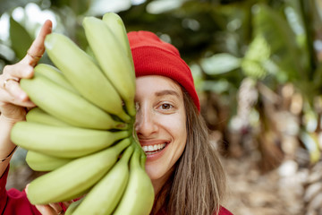 Facial portrait of a cute woman holding a stem with fresh green bananas in front of her face. Healthy eating and wellness concept