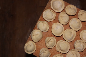 Dumplings on a wooden board. Top view on wooden table with homemade food. Uncooked handmade dumplings on a wooden plate.