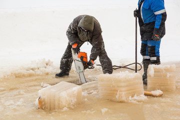 Worker in a green jacket with a hood with a chainsaw in his hands