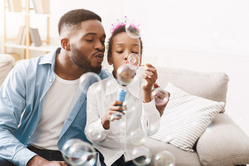 Play together. Afro father and daughter blowing soap bubbles