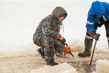 Worker in a green jacket with a hood with a chainsaw in his hands