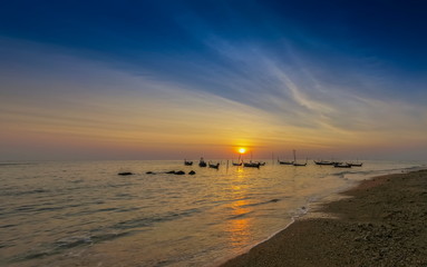 Fototapeta premium view seaside evening of fishing boats floating in the sea with orange sun light and blue sky background, sunset at Klong Hin Beach, Ko Lanta island, Krabi, southern of Thailand.